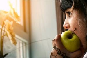 girl eats an apple and looks out the window