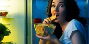 Girl eating a cracker in front of an open refrigerator