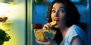 A girl eats crackers in front of an open refrigerator