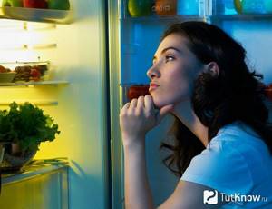 A girl with a thoughtful face looks into the refrigerator