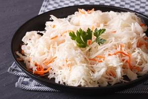sauerkraut with carrots and a sprig of parsley in a black plate on a table covered with a kitchen towel