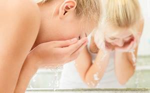 Young blonde woman washing her face with clean water