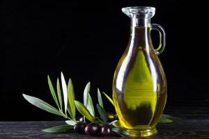 оливковое масло в графине, рядом маслины на ветке с листвой
